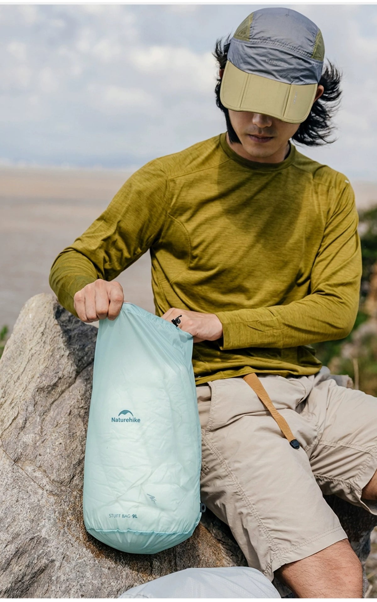 A person using the creek-blue Naturehike drawstring pouch outdoors beside a rock; the original STUFF BAG 9L marking is visible.
